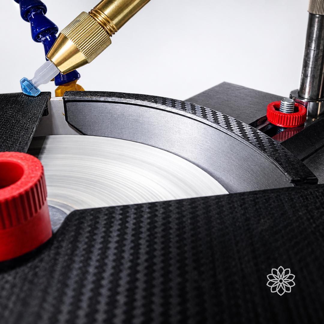 Close-up of black textured lap cover and side baffle around a spinning faceting lap with water nozzle and red thumb screws. VEVOR faceting machine accessory for splash reduction, lapidary water control, gemstone cutting, and polishing.