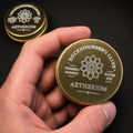 Hand holding a small engraved gold tin of Rockhounder’s Salve, showing the Aetherium logo, Founder’s Harvest batch marking, and pocket-size scale for outdoor, camping, and workshop use.