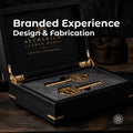 Open black wood presentation case with fitted black foam holding two custom-machined brass keys, branded Aetherium Carbon Works. White overlay reads “Branded Experience Design & Fabrication,” introducing Aetherium’s custom corporate gifting, recognition, and delivery experience service.