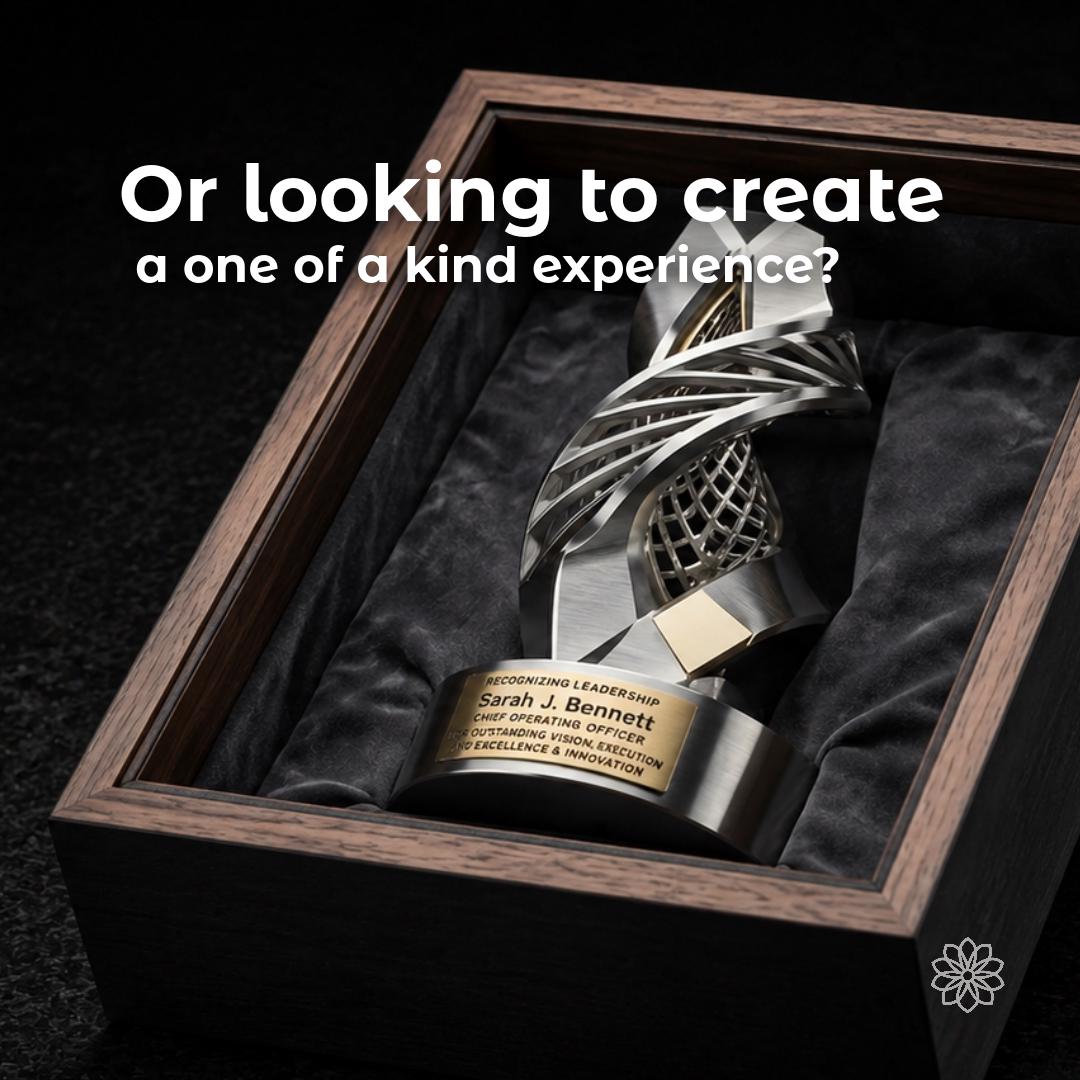 Sculptural silver-and-gold leadership award displayed in a dark walnut presentation case. Overlay asks about creating a one-of-a-kind experience, representing bespoke corporate awards and recognition pieces designed around a recipient, achievement, or company milestone.
