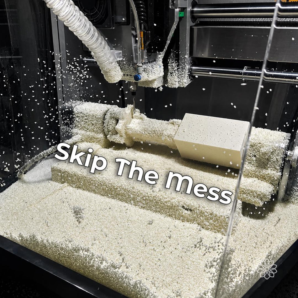 Desktop CNC enclosure filled with white machining chips around the spindle, dust hose, workholding, and workpiece, with debris visible across the cutting area.