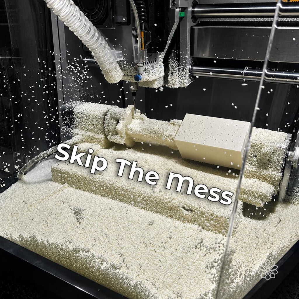 Desktop CNC enclosure filled with white machining chips around the spindle, dust hose, workholding, and workpiece, with debris visible across the cutting area.