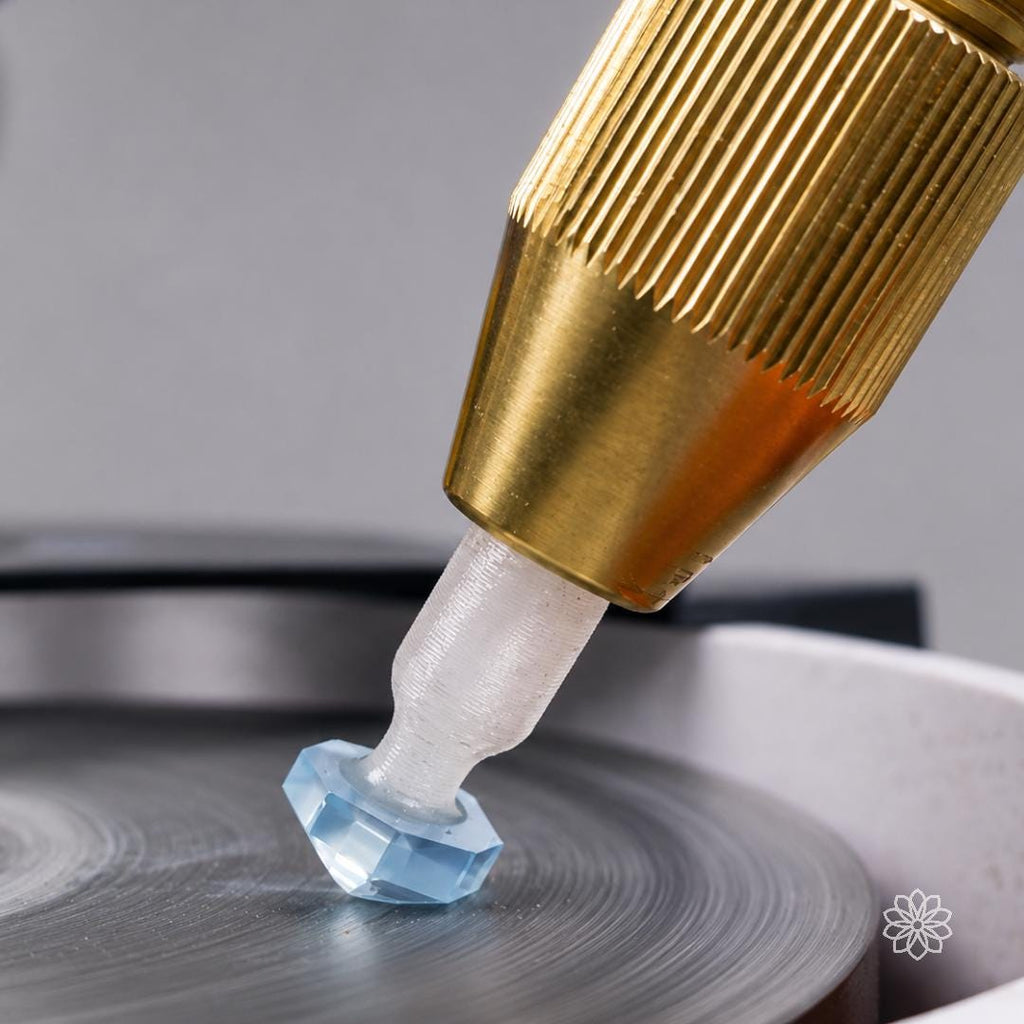 Close-up of a transparent wedge-profile polycarbonate dop holding a pale blue faceted stone against a lap. The angled dop supports the stone directionally while leaving working clearance around the gemstone during faceting and polishing.