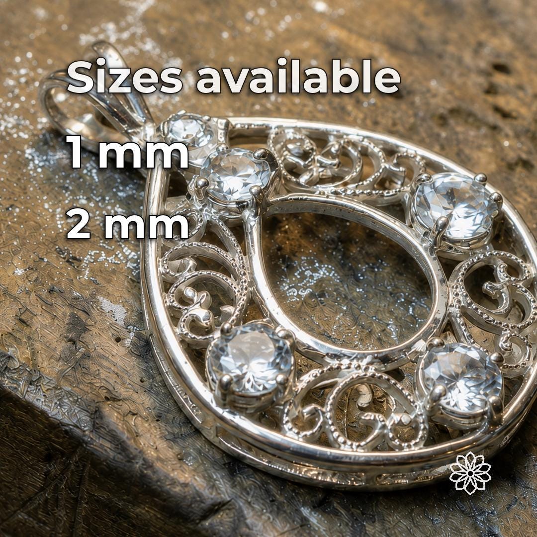 White sapphire gemstones shown set into an ornate silver jewelry piece on a working jeweler’s bench, demonstrating the bright neutral appearance of clear accent stones against polished metal. The image illustrates how white sapphire can be used for decorative settings, halos, side stones, clusters and detailed custom jewelry designs. Available loose stones are 1 mm and 2 mm.