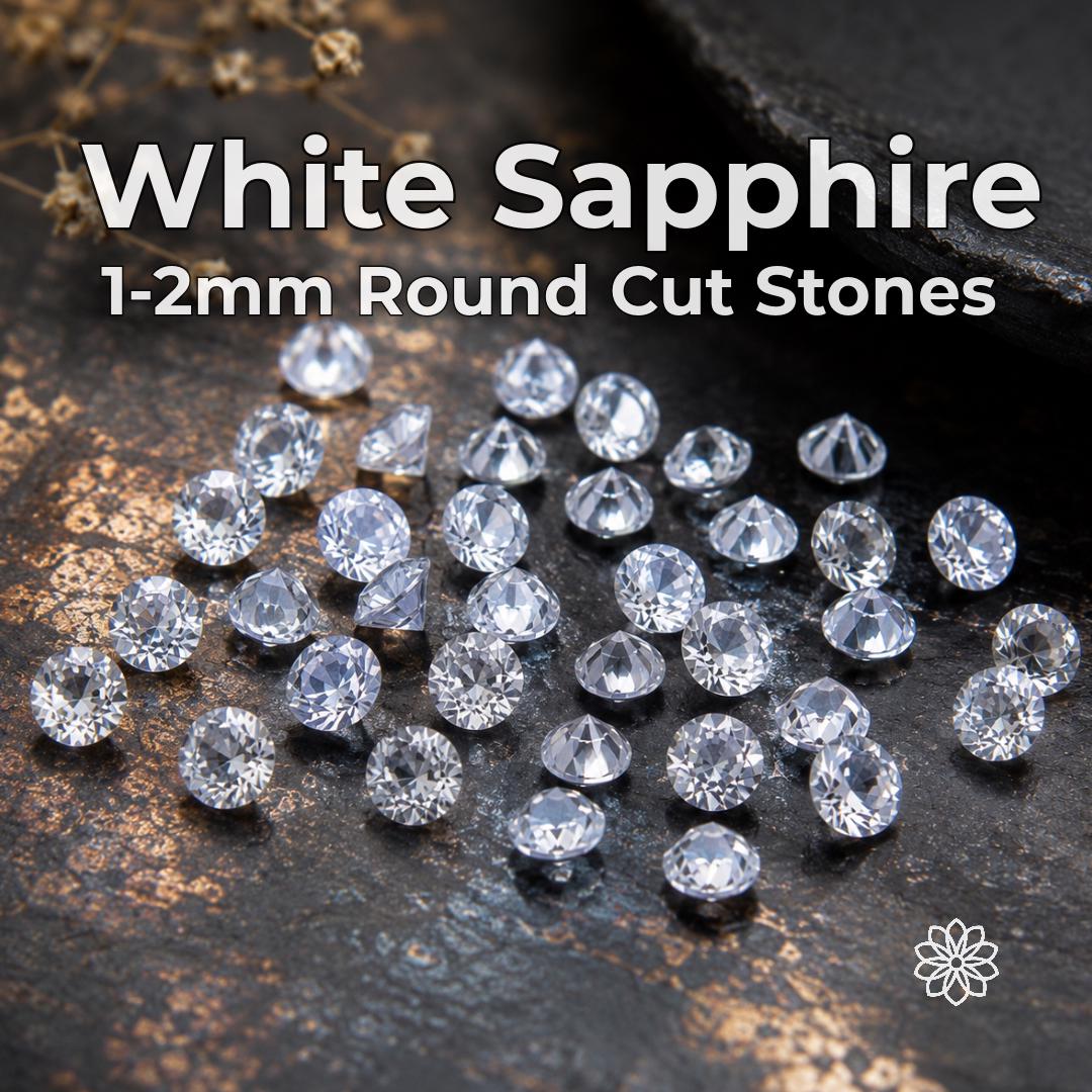 Lab-grown white sapphire gemstones in 1 mm and 2 mm round-cut calibrated sizes arranged across a dark jeweler’s work surface. Clear faceted stones are shown face-up and from the side to display brilliance, pavilion shape and cut consistency. Loose white sapphires for jewelry making, pavé, halo accents, side stones and precision settings.