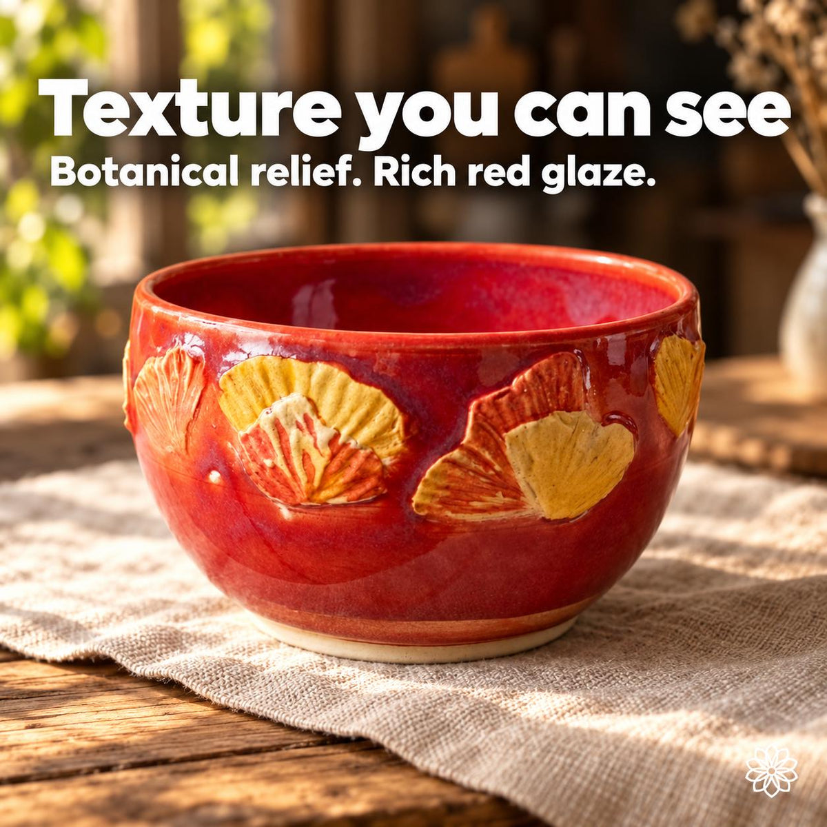 Front view of the red bowl with overlapping yellow and orange fan-shaped leaf relief above a pale foot. Text: Texture you can see. Botanical relief. Rich red glaze.