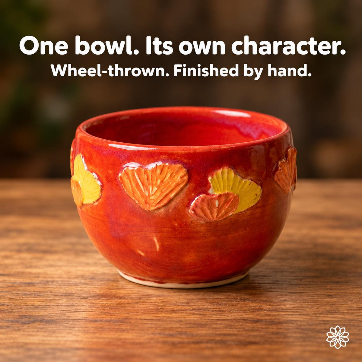Empty red ceramic bowl showing its rounded form, pale foot and carved botanical motifs from another exterior angle. Text: One bowl. Its own character. Wheel-thrown. Finished by hand.